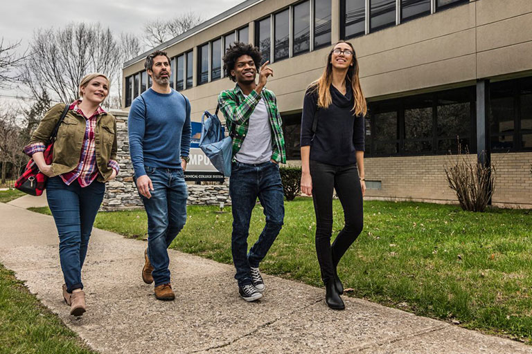 4 Students walking down campus sidewalk.