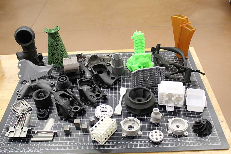3D printed parts in various colors sitting on a black mat