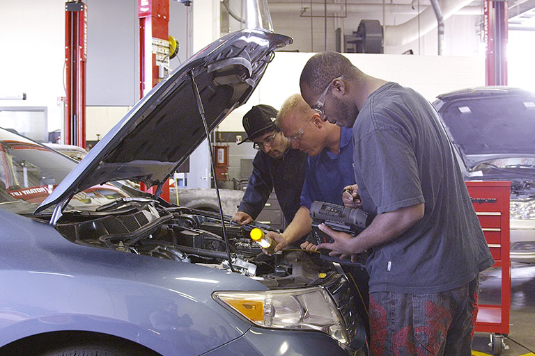 students work on a car with the hood open 