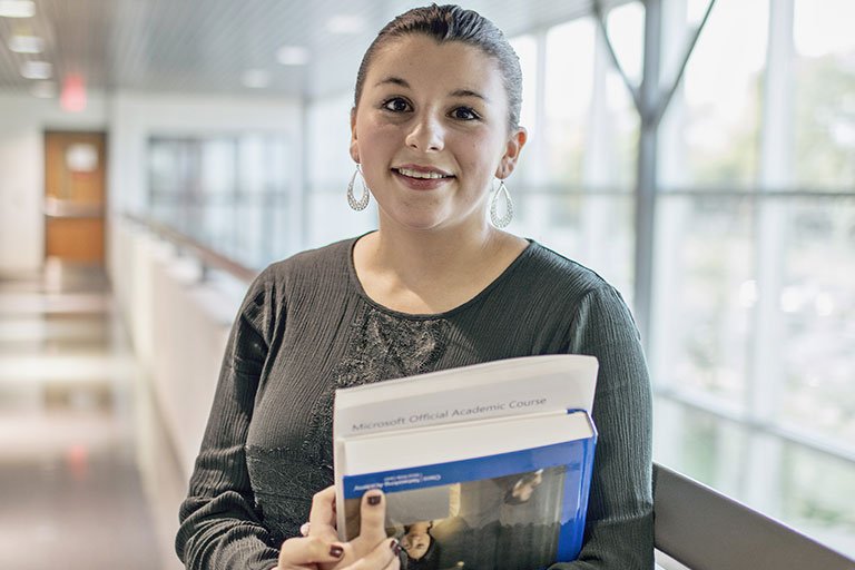 A student looking at the camera with a slight smile, while holding two textbooks