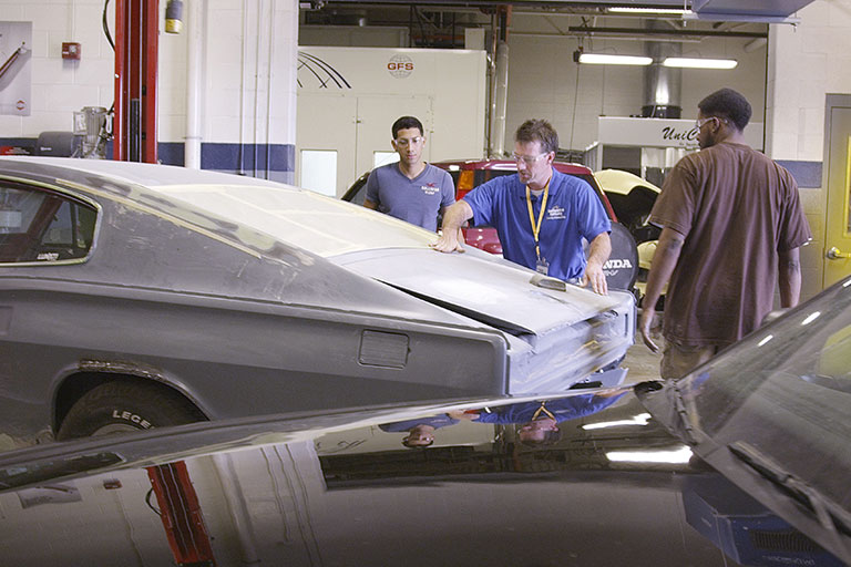 Two students and instructor inspect the back of a damaged car