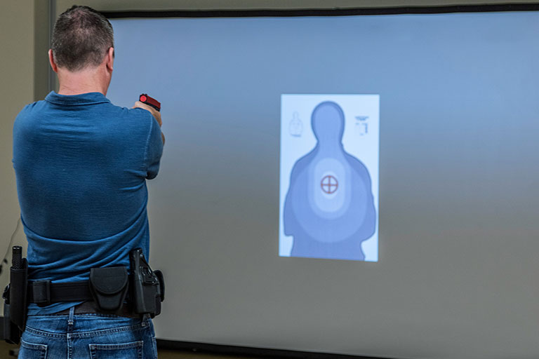 man pointing a practice gun at a target on a projector