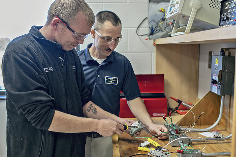 a student and an instructor working on electrical parts