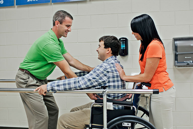 person in a wheelchair being helped up by 2 people